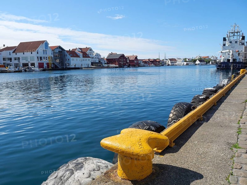Waterfront with a yellow bollard and tyre protection, water and city in the background, in sunny weather, harbour in norway with boats, ships and many houses by the sea, Haugesund, Norway, Europe