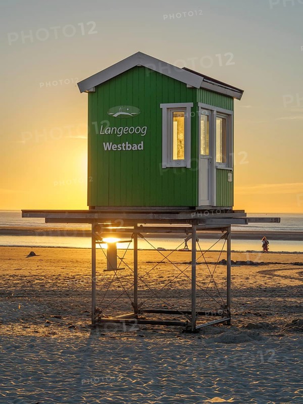 A green lifeguard hut on the beach while the sun sets in the background, evening mood on the beach with a sunset over the sea, beach chairs in the sunset, lnageoog, germany