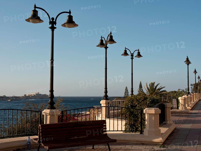 Promenade along the sea with benches, decorative lamps and palm trees, railings and clear sky, Valetta, Malta, Europe