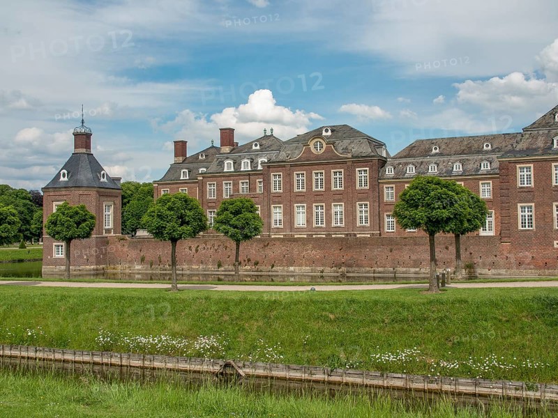 Historic brick castle with manicured lawn and trees under a cloudy sky, historic castle with a green park with sculptures and paths, nordkirchen, germany