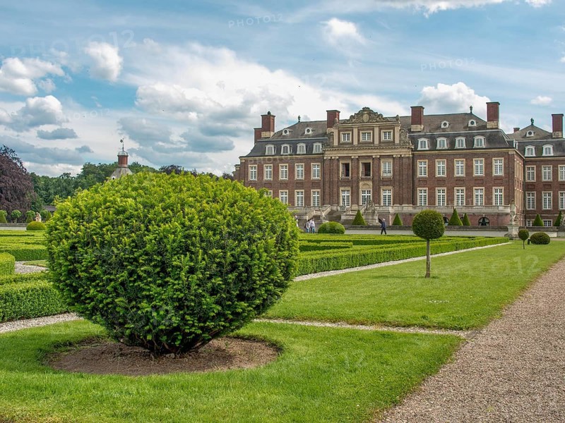 Well-kept symmetrical garden with hedges and paths in front of a historic castle under a cloudy sky, historic castle with a green park with sculptures and paths, nordkirchen, germany