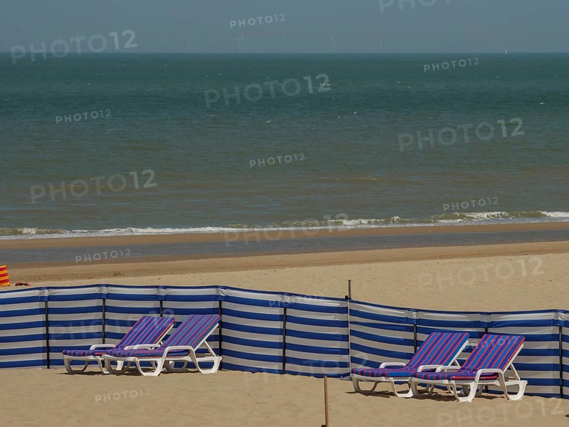 Wide view of a beach with blue and white striped deckchairs and a calm sea in the background, colourful beach loungers by the sea with blue sky, de haan, belgium