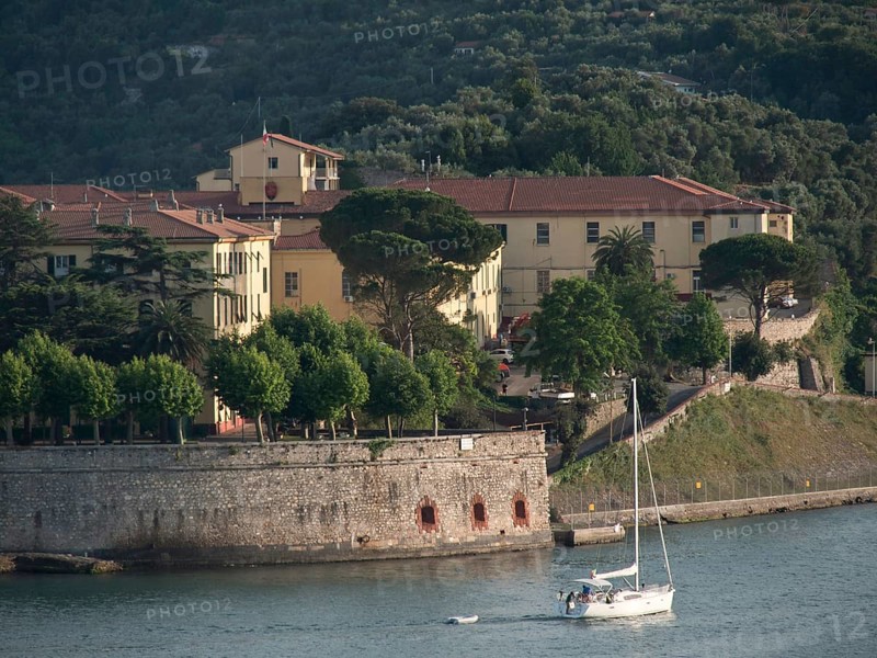 Yellow building on the waterfront, a sailboat in the foreground and forest covered hills in the background, Bari, Italy, Europe
