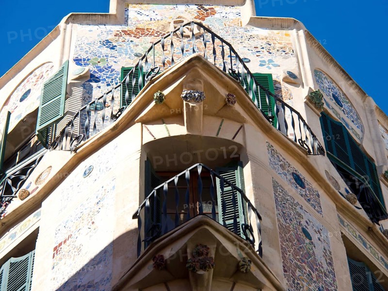 A building with decorative mosaics and balconies, green shutters and an ornate facade, palma de Majorca with its historic houses, grand cathedral and flowers, palma, spain