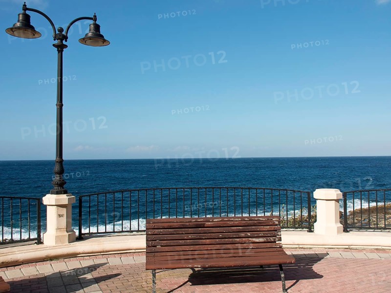 A wooden bench in front of a metal railing with sea and sky in the background, Valetta, Malta, Europe