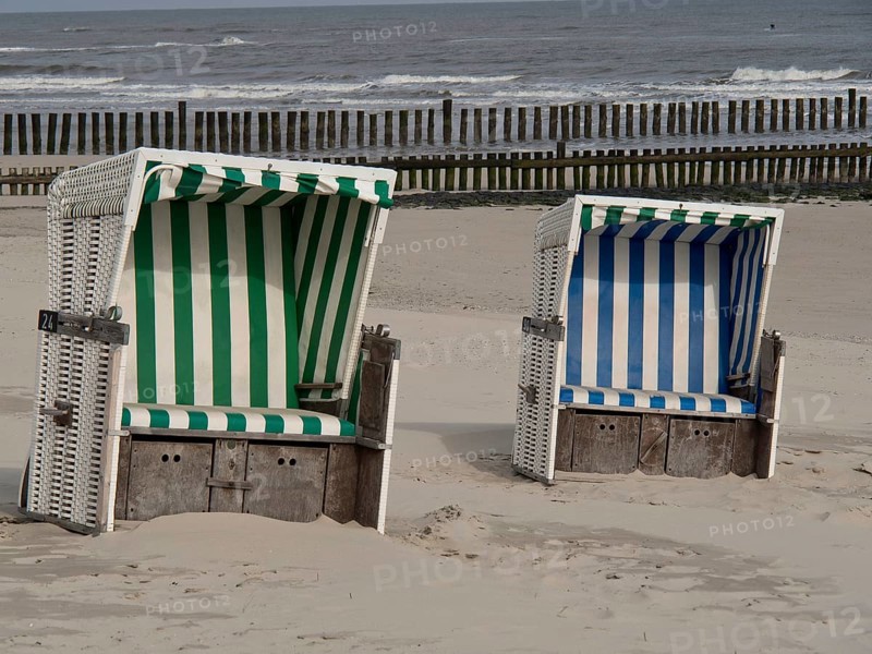 Two beach chairs, one green and white and the other blue and white striped, in front of a calm sea and sky, beach chairs on a sandy beach with North Sea waves in the background, wangerooge, Germany, Europe
