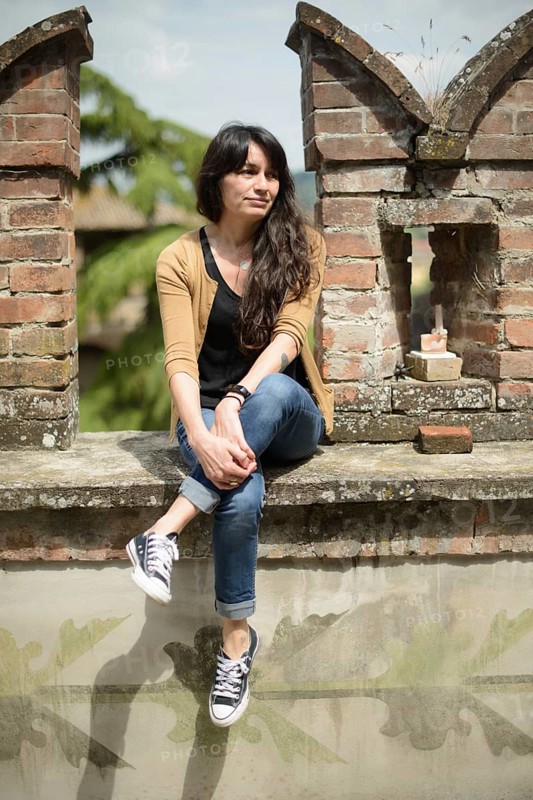 Thoughtful young woman sits on an old brick wall, casually dressed, enjoying a peaceful moment in a rustic outdoor setting