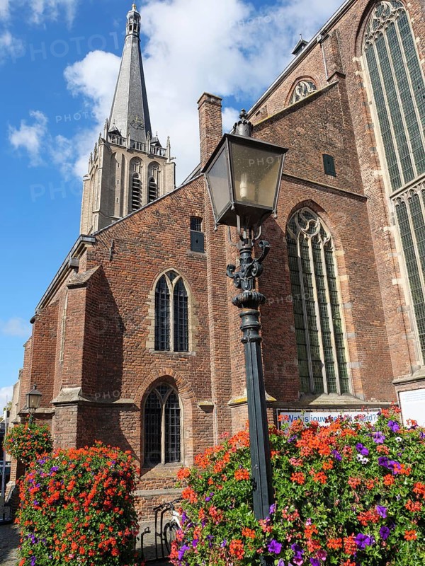 Historic red brick gothic church with high steeple, a large flower bed and lamppost under a blue sky, red brick houses and churches in the Netherlands, Doesburg, Netherlands