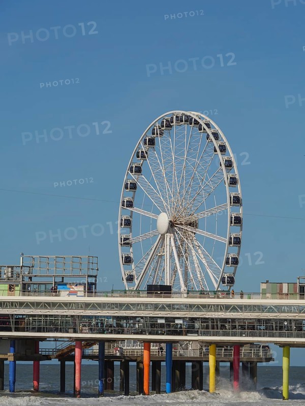 Ferris wheel on a pier reaching into the sea under a blue sky, parasols and a pier on the beach of Scheveningen, Scheveningen, Netherlands