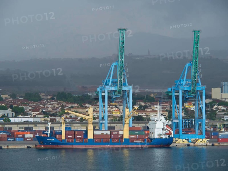 A freighter stands in the harbour with large blue cranes and many containers in the background, Marseille on the Mediterranean Sea with the old cathedral and ships in the historic harbour, rocky coast on the Mediterranean Sea, marseille, france