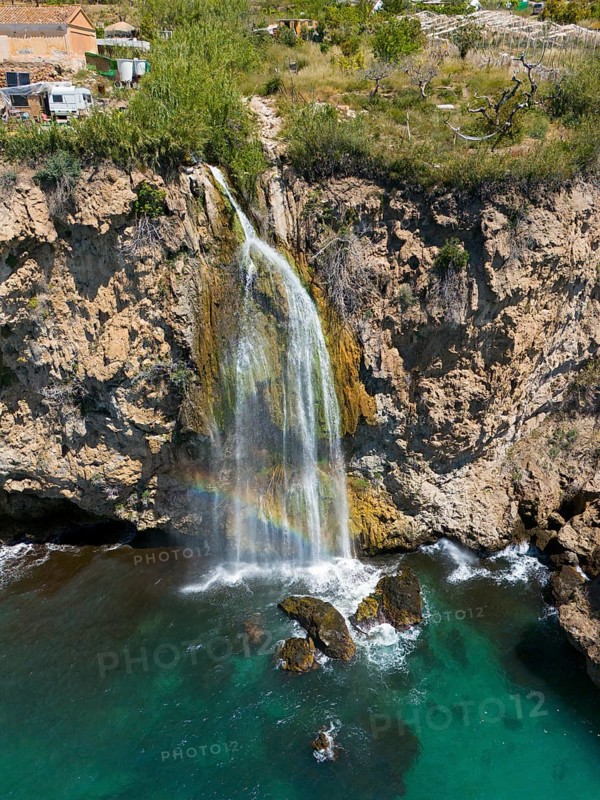 A waterfall cascades from a cliff into turquoise-coloured water in a rocky, natural setting, aerial view, Cascada Grande de Maro, Nerja, Malaga, Andalucia, Spain, Europe