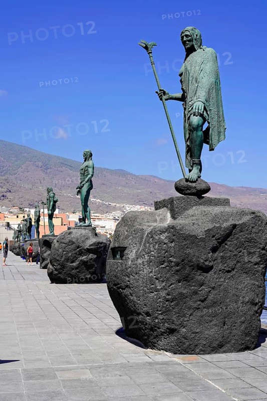 Statues of the Guanche Kings or Mencey Statues, in front Guanche King Adjona, promenade of Candelaria, Tenerife, Canary Islands, Spain, Europe, Historical bronze statue on stone pedestal along a coastal promenade with mountain landscape in the background, Europe