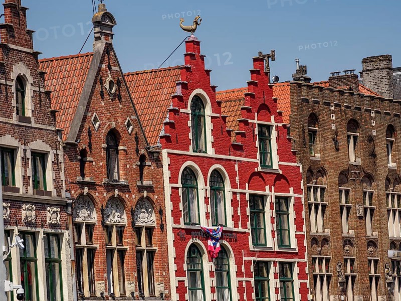 Row of colourful historic houses with gabled roofs and large windows under a clear blue sky, historic house facades in a medieval riverside town, Bruges, Belgium, Europe