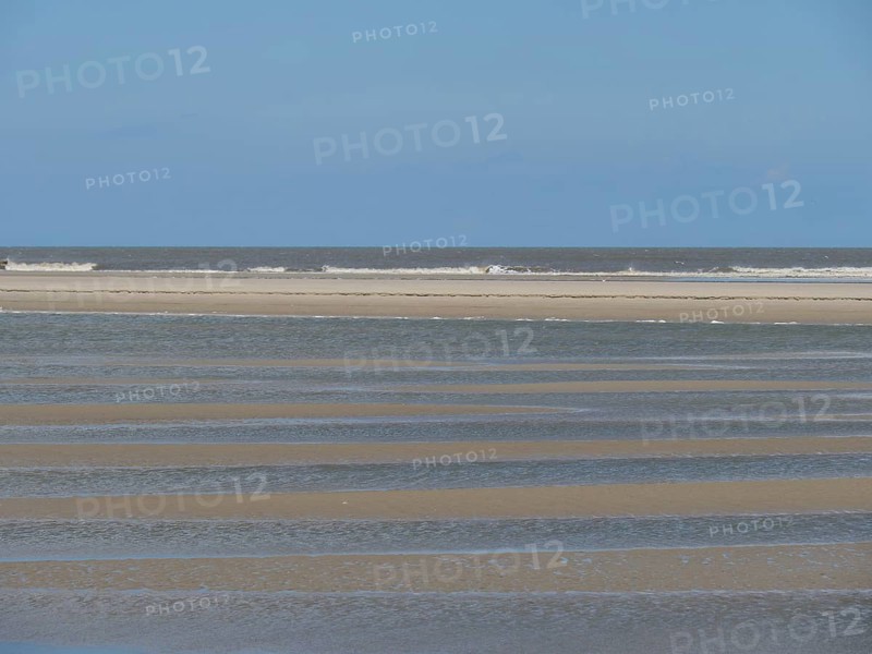 Empty beach at low tide with strips of sand and water under a blue sky, Baltrum Germany