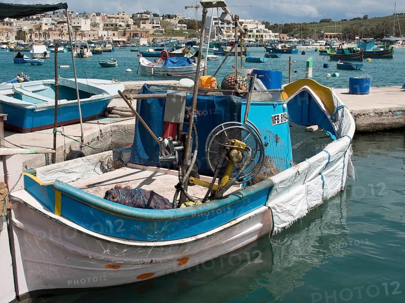 A fishing boat with various items of equipment in the harbour, many colourful fishing boats in a small harbour against a historical backdrop, Marsaxlokk, malta