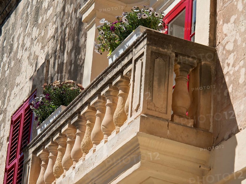 A small balcony with flowers and shutters adorns an old stone wall, the town of mdina on the island of malta with historic houses, colourful balconies, magnificent churches, mdina, Malta, Europe