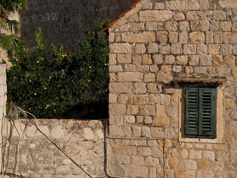 Detailed view of a stone wall with shutters framed by mediterranean vegetation, the old town of Dubrovnik with historic houses, churches, red roofs and fortress walls, dubrovnik, coratia