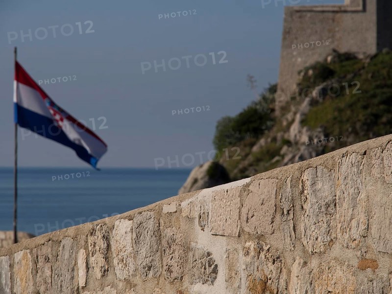 Croatian flag flying next to a historic fortress, overlooking the sea and the clear blue sky, the old town of Dubrovnik with historic houses, churches, red roofs and fortress walls, dubrovnik, coratia