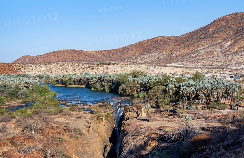 Kunene River with green vegetation in dry red mountain landscape, waterfall and African Baobab (Adansonia digitata), in the evening light, Epupa Falls, Kunene, Namibia, Africa