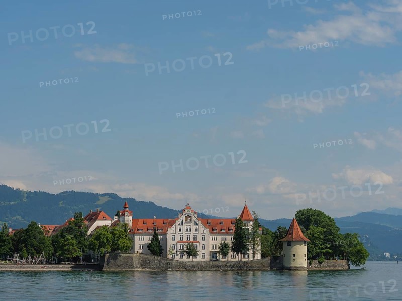 A castle with red roofs on a lake, surrounded by trees and mountains in the background, view of a lakeside town with lighthouse and church towers, Lindau, Germany, Europe