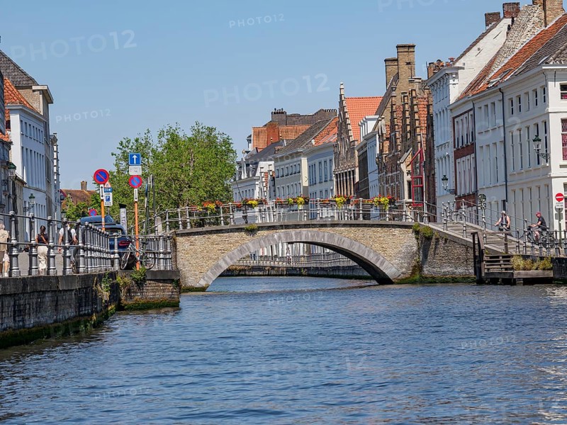 Canal with stone bridge and colourful flowers, flanked by historic houses and lively city life on a sunny day, historic city on the river with ornate gables, old facades and historic towers, Bruges, Belgium, Europe