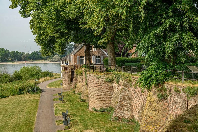 An old house on a river bank with garden and green trees, wall in the foreground, summer ambience, the promenade of Rees on the Rhine with green trees in spring, Rees, Germany, Europe