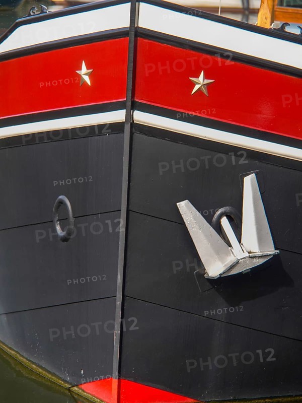 Detailed view of the bow of a black painted ship in the harbour with a large anchor, historic houses in Hoorn and ships in the harbour, hoorn, the netherlands