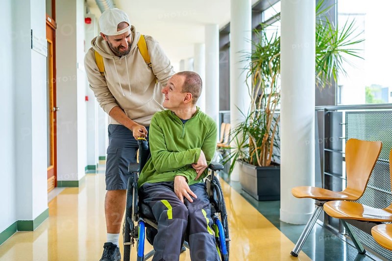 Caucasian young man pushing the wheelchair of a friend with disability around the university