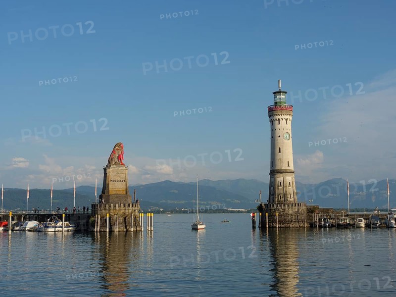 Panoramic view of the harbour with a lighthouse and lion sculpture under a blue sky, towers at a harbour on the lake with sailing boats, Lindau, Germany, Europe