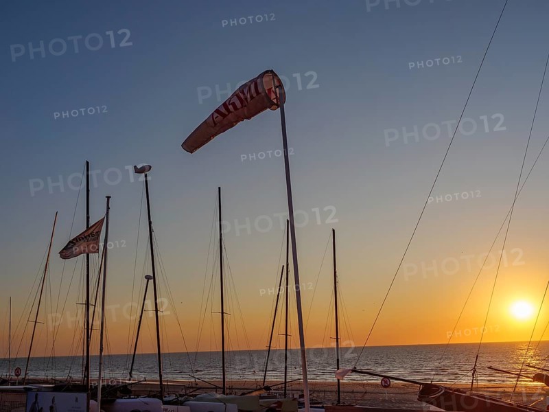 Sunset at the beach harbour with several sailing boats and waving flags, calm sea and clear sky, sunset in many colours at the beach with a calm sea, de haan, belgium
