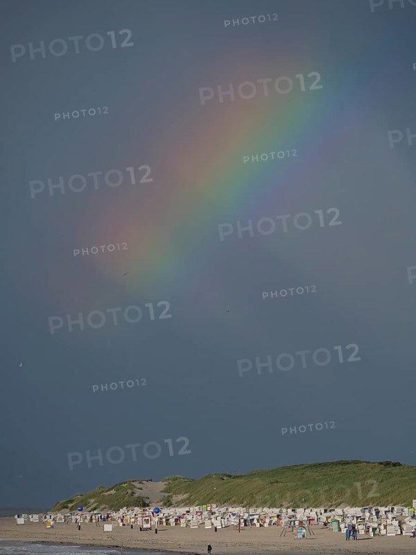 A rainbow appears in the dark sky above a beach, Baltrum Germany