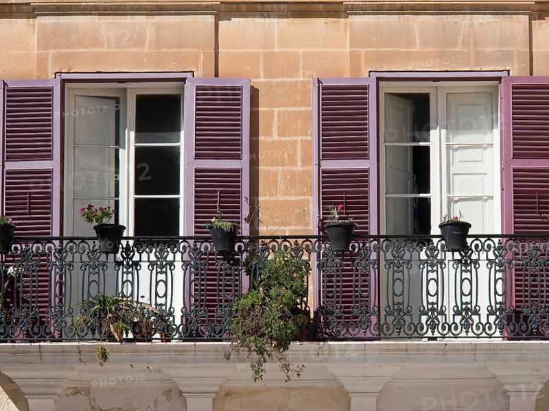 A mediterranean balcony with purple shutters and potted plants in front of two open windows, the town of mdina on the island of malta with historic houses, colourful balconies, magnificent churches, mdina, Malta, Europe