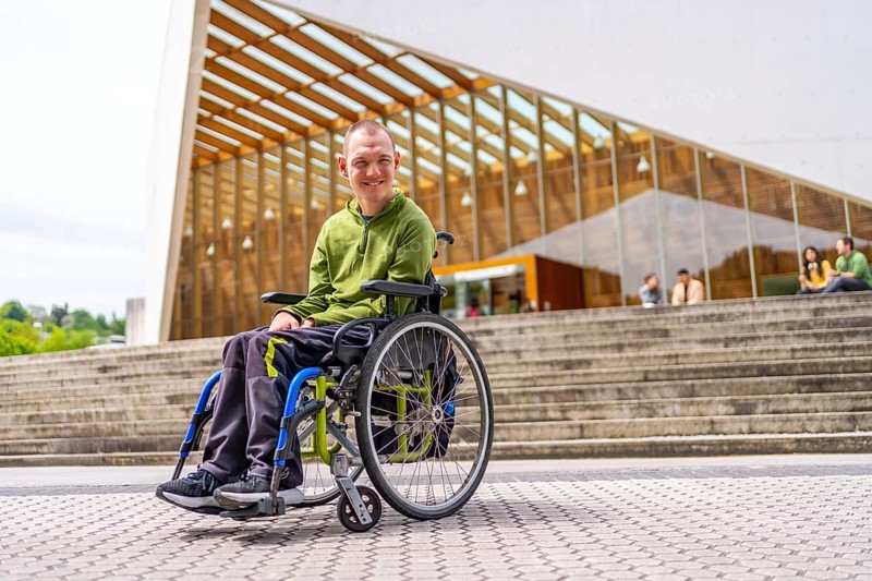Full length low angle view portrait of a happy caucasian adult man with cerebral palsy smiling proud outside the university