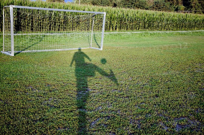 Shadow of a Soccer Player and Playing the Ball to the Goal Close to a Corn Field in a Sunny Day in Switzerland