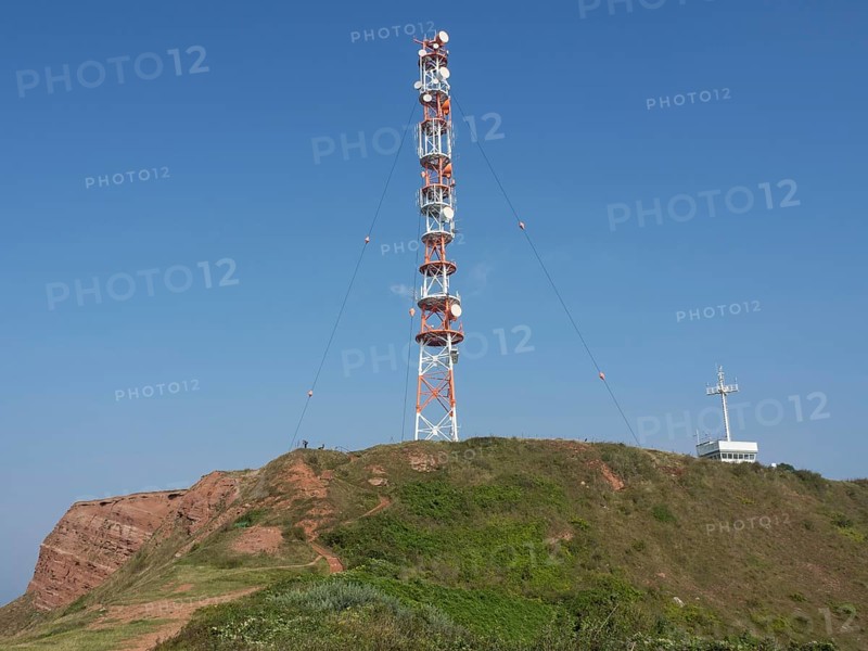 A large transmission mast stands on an overgrown hill under a clear sky. A technical highlight in nature, Heligoland, Germany, Europe
