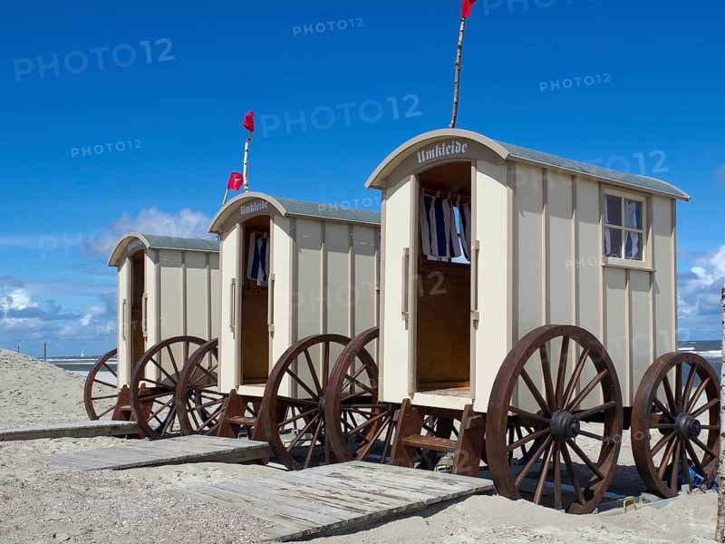 Beach with changing cabins and people on the shore, red flags and blue sky in the background, historic bathing carts on the sandy beach in front of a blue sky, Norderney, Germany, Europe