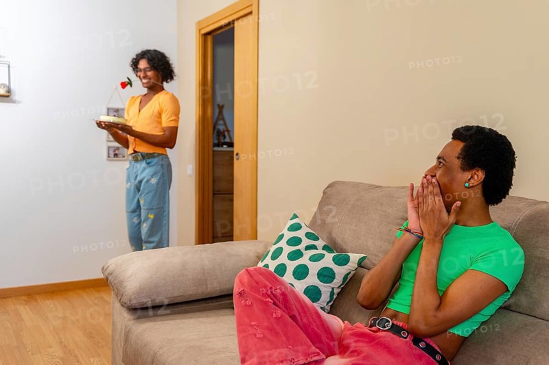 Gay latin young man surprising his partner with cake and a rose at home
