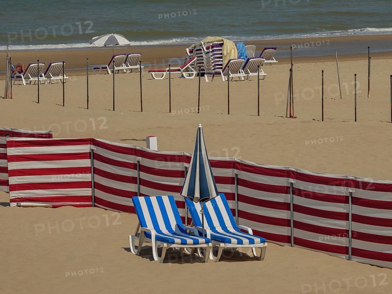 Empty beach with scattered blue and white striped deckchairs, parasols, red partitions and sea view, colourful beach loungers by the sea with blue sky, de haan, belgium