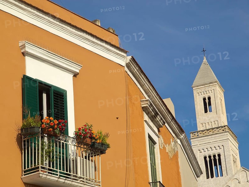 Colourful facade with green shutters, balcony with flowers and a church tower against a clear blue sky, The city of Bari on the Mediterranean with historic buildings, small boats in the harbour and beautiful churches and the old fortress, bari, italy