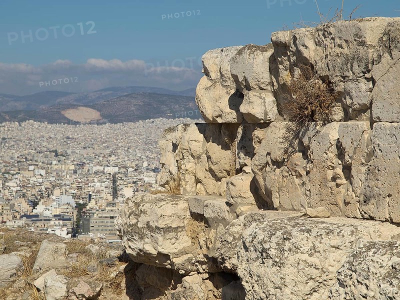 Large ancient stones on a hill overlooking a modern city under a blue sky, Ancient buildings with columns and trees on the Acropolis in Athens against a blue sky, athens, greece