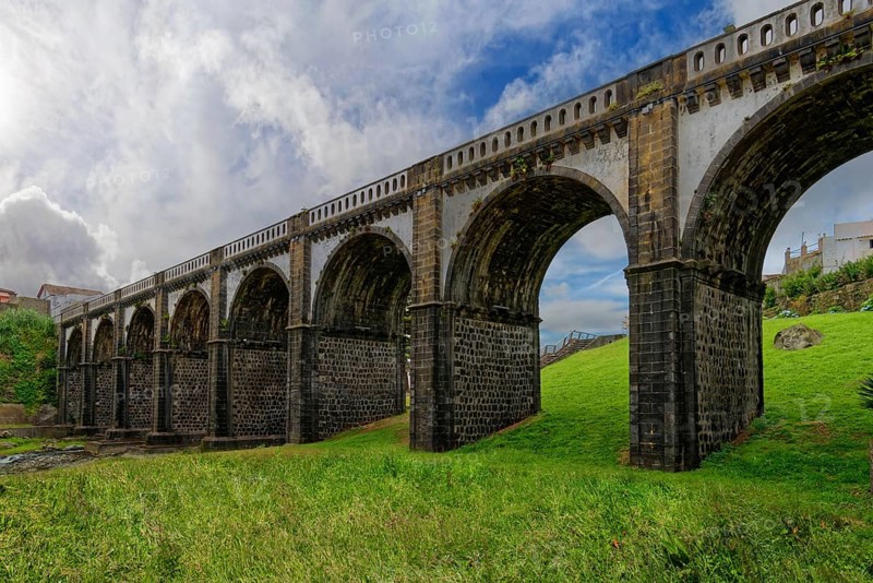 Historic majestic eight-arched bridge over the Ribeira Grande river against a backdrop of grass and clouds, coastal town of Ribeira Grande, Santa Barbara, Sao Miguel, Azores, Portugal, Europe
