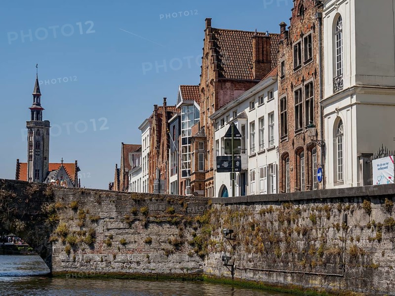 Stone bridge and historic facades with a view of a church tower along a canal under a blue sky, historic city by the river with ornate gables, old facades and historic towers, Bruges, Belgium, Europe