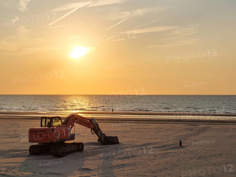 A dredger in warm light on the beach during sunset, facing the calm sea, sunset on the beach of de haan on the north sea, de han, belgium