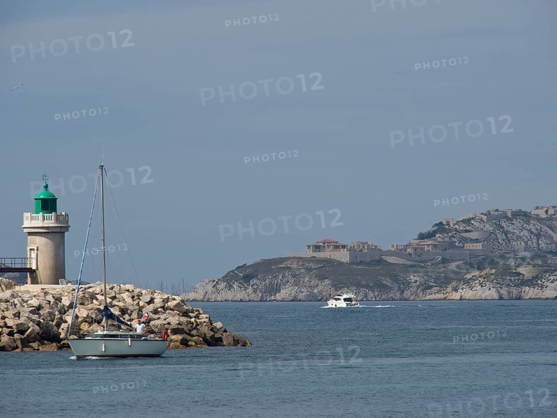 A lighthouse and boats on calm waters off a rocky coast, Marseille on the Mediterranean Sea with the old cathedral and ships in the historic harbour, rocky coast on the mediterranean sea, marseille, france