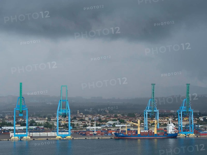 Large blue harbour cranes lifting containers, cloudy sky and a ship in the harbour industrial area in the background, Marseille on the Mediterranean Sea with the old cathedral and ships in the historic harbour, rocky coast on the Mediterranean Sea, marseille, france