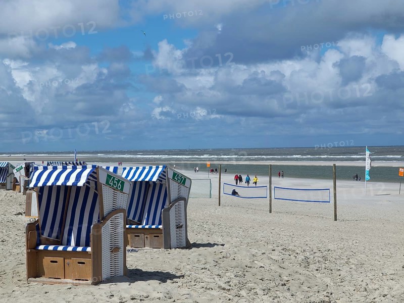 Blue and white beach chairs on the beach with people in the background in sunny weather, clouds on the beach of Noderney in front of colourful beach chairs and waves in the sea, Nordereney, Germany, Europe