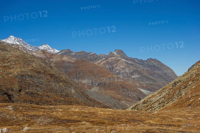 Vast valley between rocky mountains and mountain range under a bright blue sky, bare mountain peaks with blue sky, saas fee, switzerland
