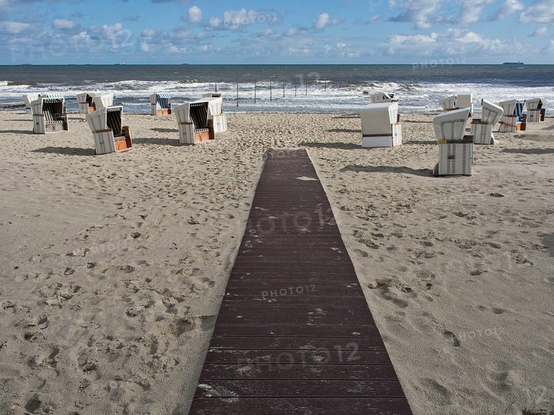 A wooden path leads to scattered white beach chairs on the sandy beach on a blue sky day with clouds, beach chairs on the sandy beach of Wangerooge on the North Sea, Wangerooge, germany