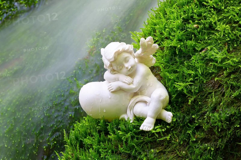 Porcelain angel figurine on moss by a waterfall