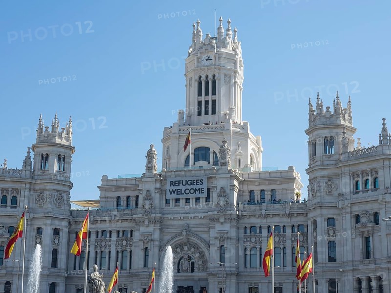 Magnificent white palace with towers, Spanish flags and a welcome banner for refugees, Madrid, Spain, Europe